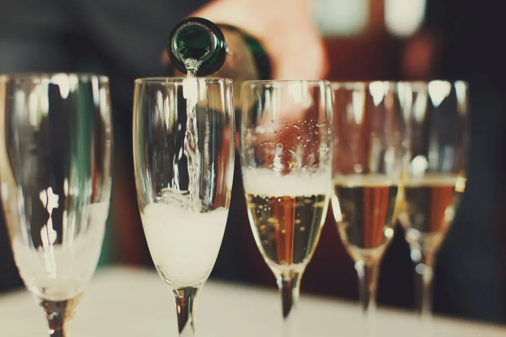 Close up of row of champagne glasses being filled by a bottle